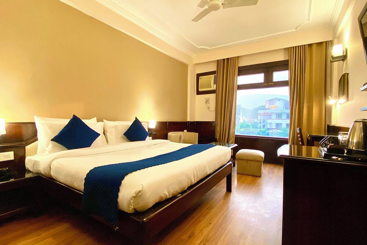 A hotel room with a large bed, bedside tables, a desk with a chair, a television, and a window with curtains.