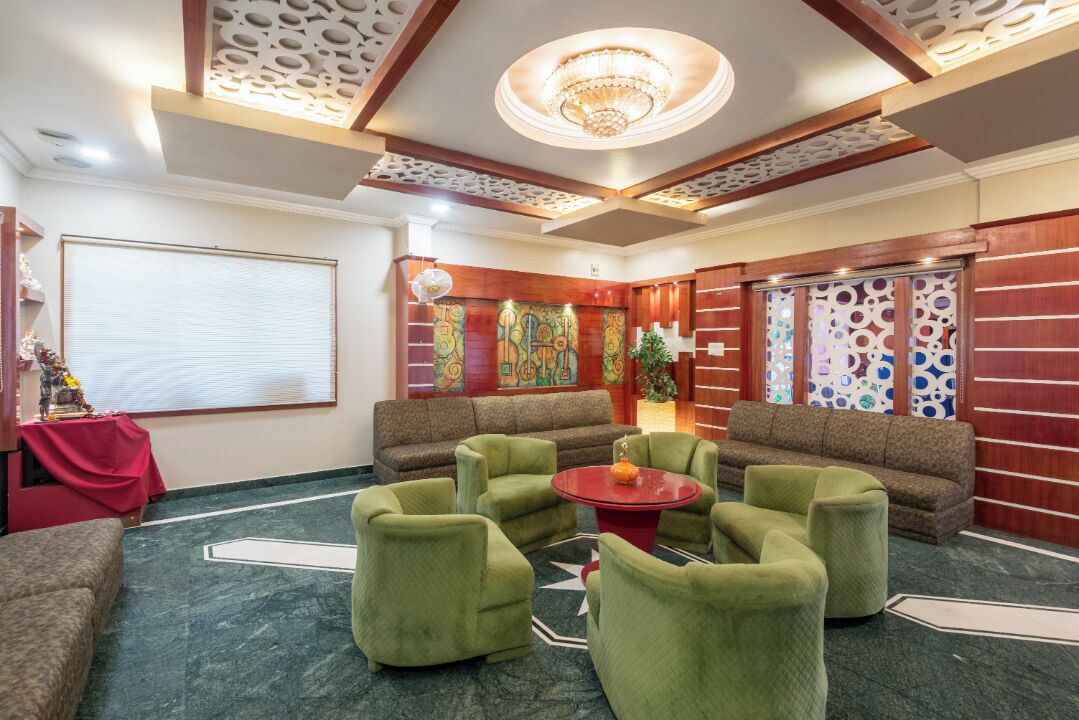 A lobby with green armchairs, a red table, and a chandelier.