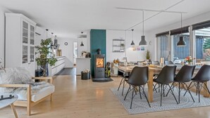 Une cuisine moderne dotée d’un îlot central, un coin repas avec une grande table et des chaises, et un espace salon confortable avec un canapé et une table basse.