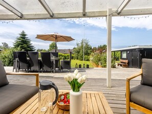 Une terrasse extérieure avec une table, des chaises, une cafetière et un vase de fleurs.