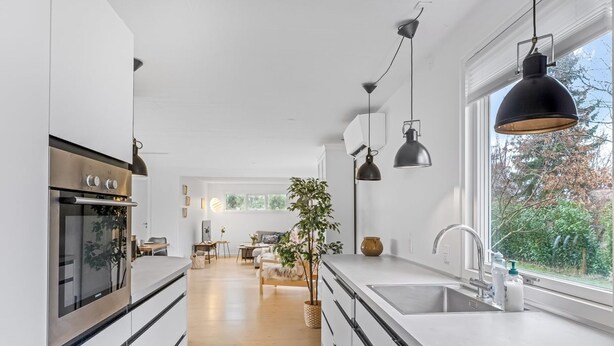 Une cuisine moderne dotée d’un grand îlot central, d’appareils électroménagers en acier inoxydable, de luminaires suspendus et offrant une vue sur l’espace de vie.