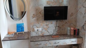 Un salón moderno con un televisor de pantalla plana montado en una pared de mármol, un espejo redondo y una mesita con un cuadro y libros.