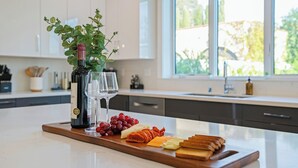 A kitchen island with a wine bottle, glasses, grapes, cheese, and bread.