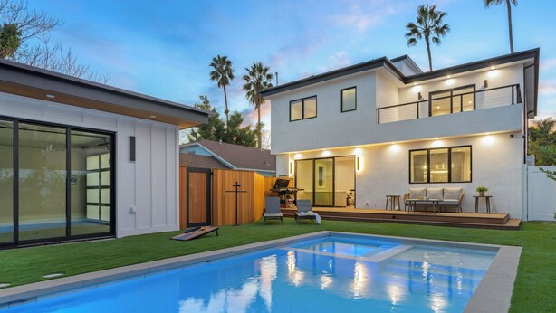 A modern two-story house with a swimming pool, large windows, and a well-maintained lawn.
