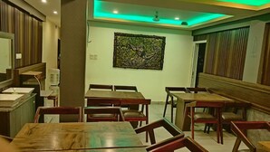 A restaurant with wooden tables and chairs, a water dispenser, and a decorative wall piece. - Seven Seas Dream Castle Port Blair (Port Blair)