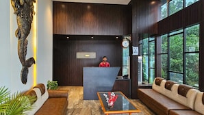 A reception area with a receptionist, a reception desk, a sofa, a coffee table, and a large window with a view of greenery. - Seven Seas Dream Castle Port Blair (Port Blair)