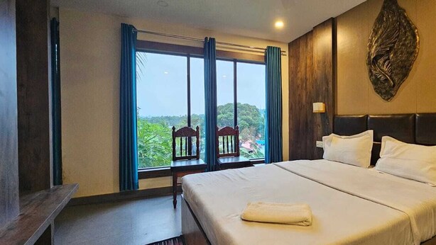 A hotel room with a large bed, two windows with curtains, a wooden headboard, and a wall-mounted light fixture. - Seven Seas Dream Castle Port Blair (Port Blair)