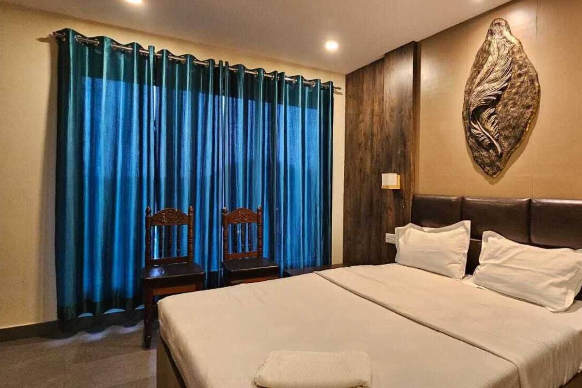 Une chambre d’hôtel avec un grand lit, deux tables de chevet, une lampe fixée au mur et un rideau.