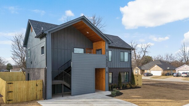 A two-story modern house with a wooden staircase, a fenced yard, and a clear sky. - Madison's Masterpiece in Downtown Tulsa-Sleeps 6 (Tulsa)