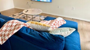 Un salon avec un canapé bleu, une petite table ronde et un téléviseur fixé au mur.