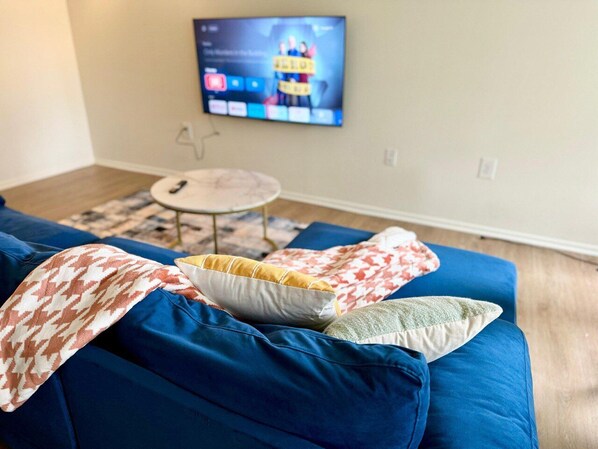 A living room with a blue sofa, a small round table, and a television mounted on the wall.