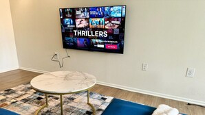 Un salon avec un téléviseur à écran plat affichant l’interface de Netflix, une table ronde et un tapis à motifs.
