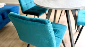 Een eethoek met smaragdgroene stoelen en een ronde tafel.