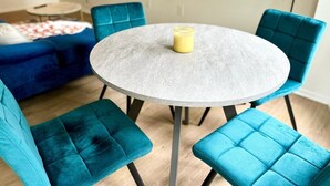 Une table ronde dont le plateau présente une surface texturée de couleur grise, entourée de quatre chaises recouvertes d’un tissu turquoise.