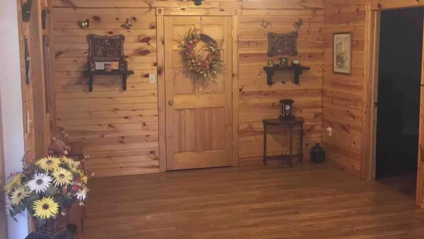 Un intérieur en bois avec une porte en bois, une guirlande, une petite table et un vase de fleurs.