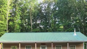 Une maison à deux étages avec un toit en métal vert, un porche à l’avant doté de quatre chaises et une allée gravillonnée.