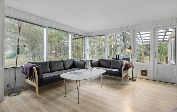 Un salon moderne avec un canapé d’angle, une table basse ronde et de grandes fenêtres donnant sur l’extérieur.