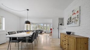 A modern kitchen with a large dining table, black chairs, a wooden cabinet, and a white brick wall with artwork. - Stunning home in Nexø with WiFi (Nexø)
