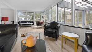 A spacious living room with a large window, a black leather sofa, a black armchair, and a small round table. - Stunning home in Nexø with WiFi (Nexø)