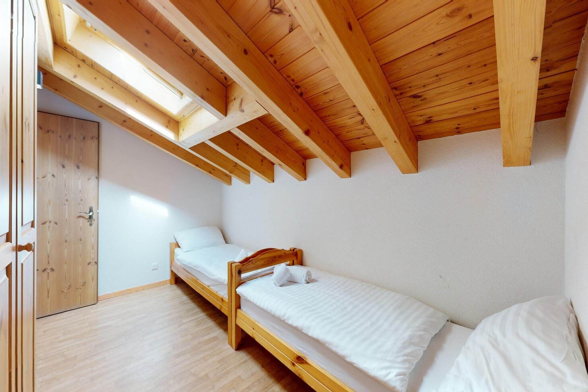A small, single-bed room with a sloped ceiling and wooden beams, a wooden wardrobe, and a skylight.
