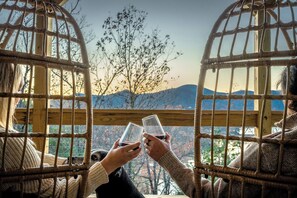 Two people sitting in wicker chairs with a view of trees and mountains through a wooden railing. - Epic Lake Views, Hot Tub, Fire Pit & Game Room (Lake Lure)