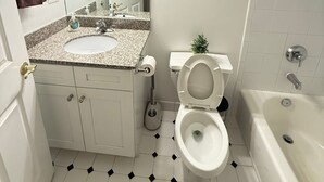 Ein Badezimmer mit einem weißen Waschbecken, einer Toilette und einer Badewanne. Ein Handtuchhalter mit einem braunen Handtuch ist angebracht.