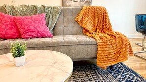 Ein Wohnzimmer mit grauem Sofa, einem runden Couchtisch, einer Topfpflanze und einem blauen, gemusterten Teppich.