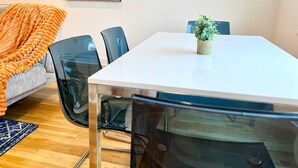Ein Essbereich mit einem weißen Tisch, schwarzen Stühlen, einem blauen Teppich und einem kleinen Topfpflanzen.