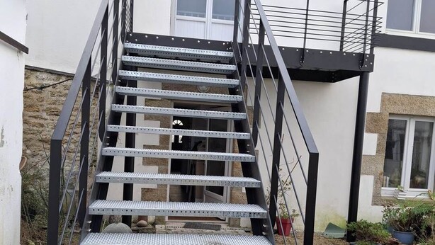 Een metalen trap die leidt naar een woongebouw met een witte gevel en een klein balkon.