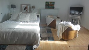 Een slaapkamer met een bed, nachtkastje, televisie, schilderij en stoel.