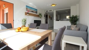 Un salon moderne avec un coin repas, comprenant une table à manger en bois, des canapés gris et un téléviseur à écran plat.