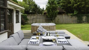 An outdoor dining area with a table set for four, surrounded by grey sofas, and a hot tub in the background. - The Old Rectory (Tring)