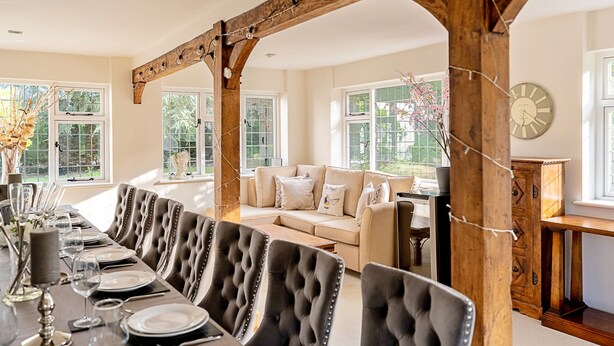 A dining area with a long table set for six, upholstered chairs, and a wooden ceiling structure. - The Old Rectory (Tring)