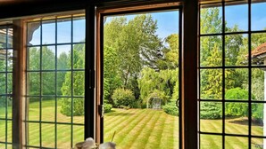 A view through a window with a grid pattern, revealing a well-maintained garden with a lawn, various shrubs, and trees. - The Old Rectory (Tring)