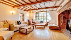 A spacious living room with wooden flooring, a fireplace, and a large window providing natural light. - The Old Rectory (Tring)