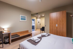 Habitación de hotel con cama, escritorio, silla, armario de madera y un pequeño banco.