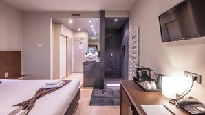 A hotel room with a bed, a desk with a phone, a TV, and a shower area. - Falko Hotel (Meise)