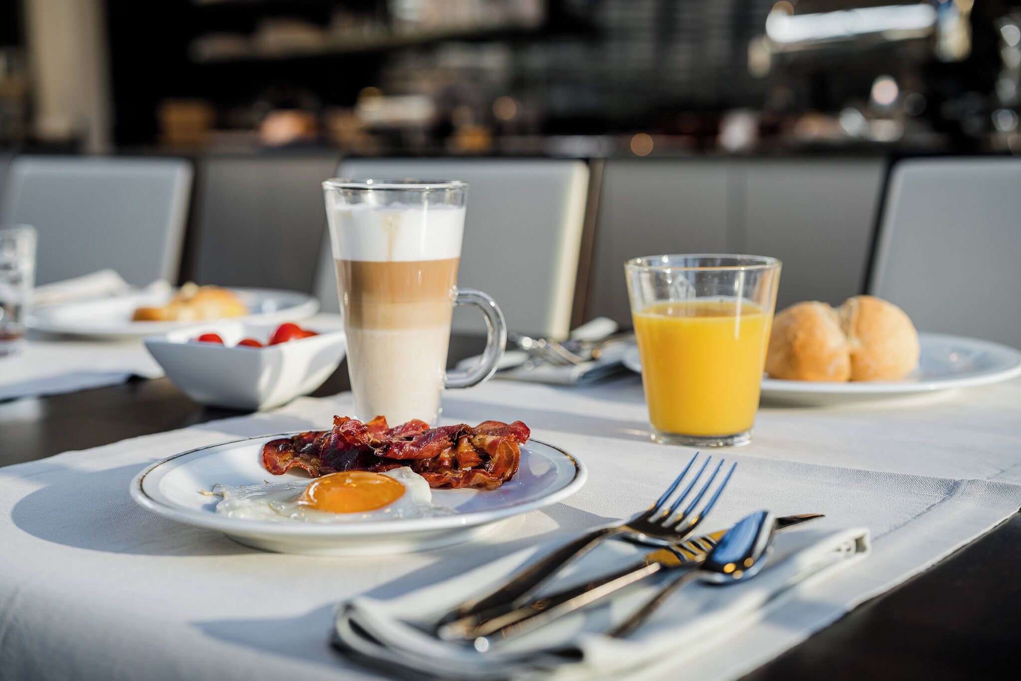 Desayuno con tocino, un huevo, una bebida de café alta y un vaso de jugo de naranja.
