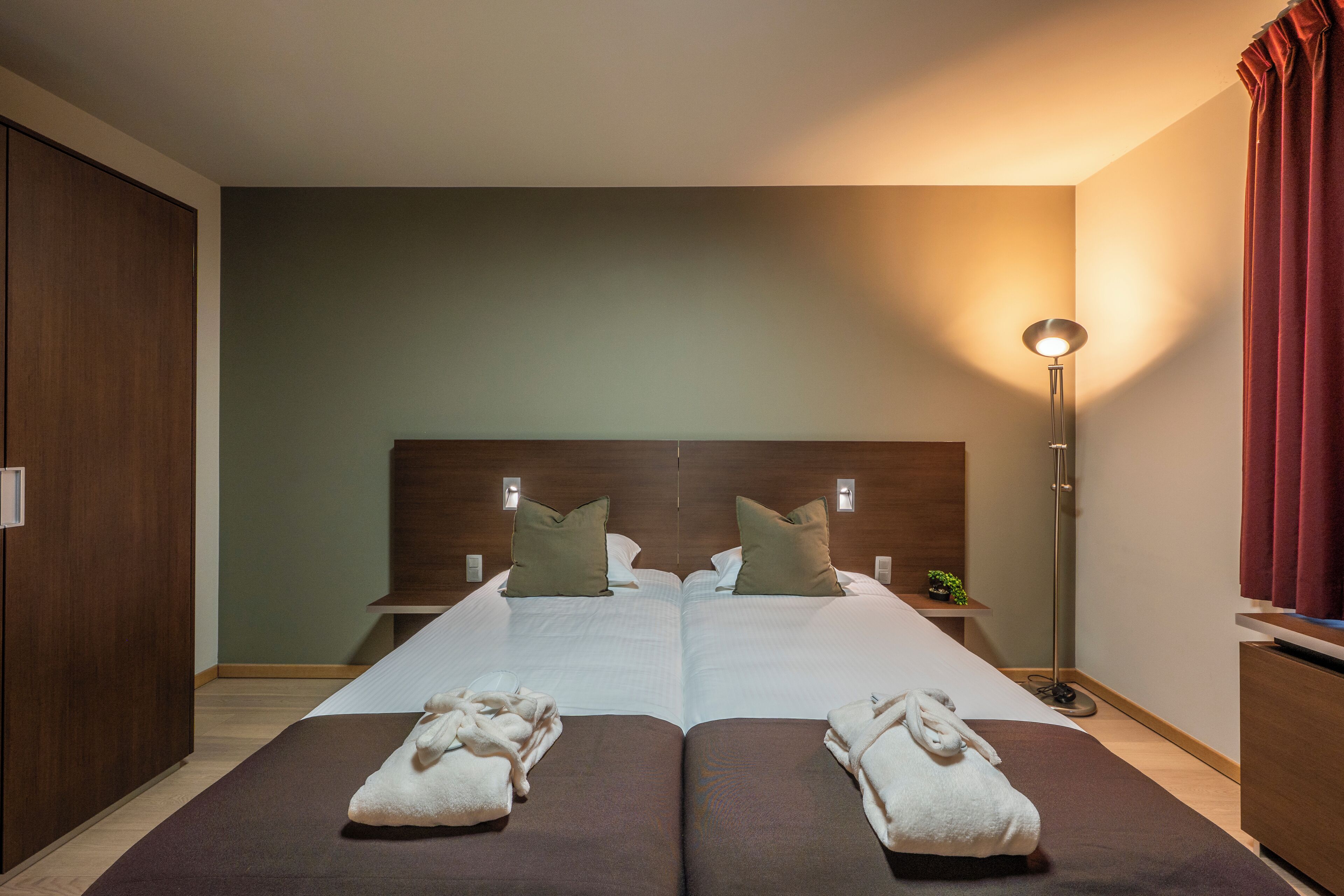 A double bed with two pillows, a bedside table with a lamp, and two towels on the floor.