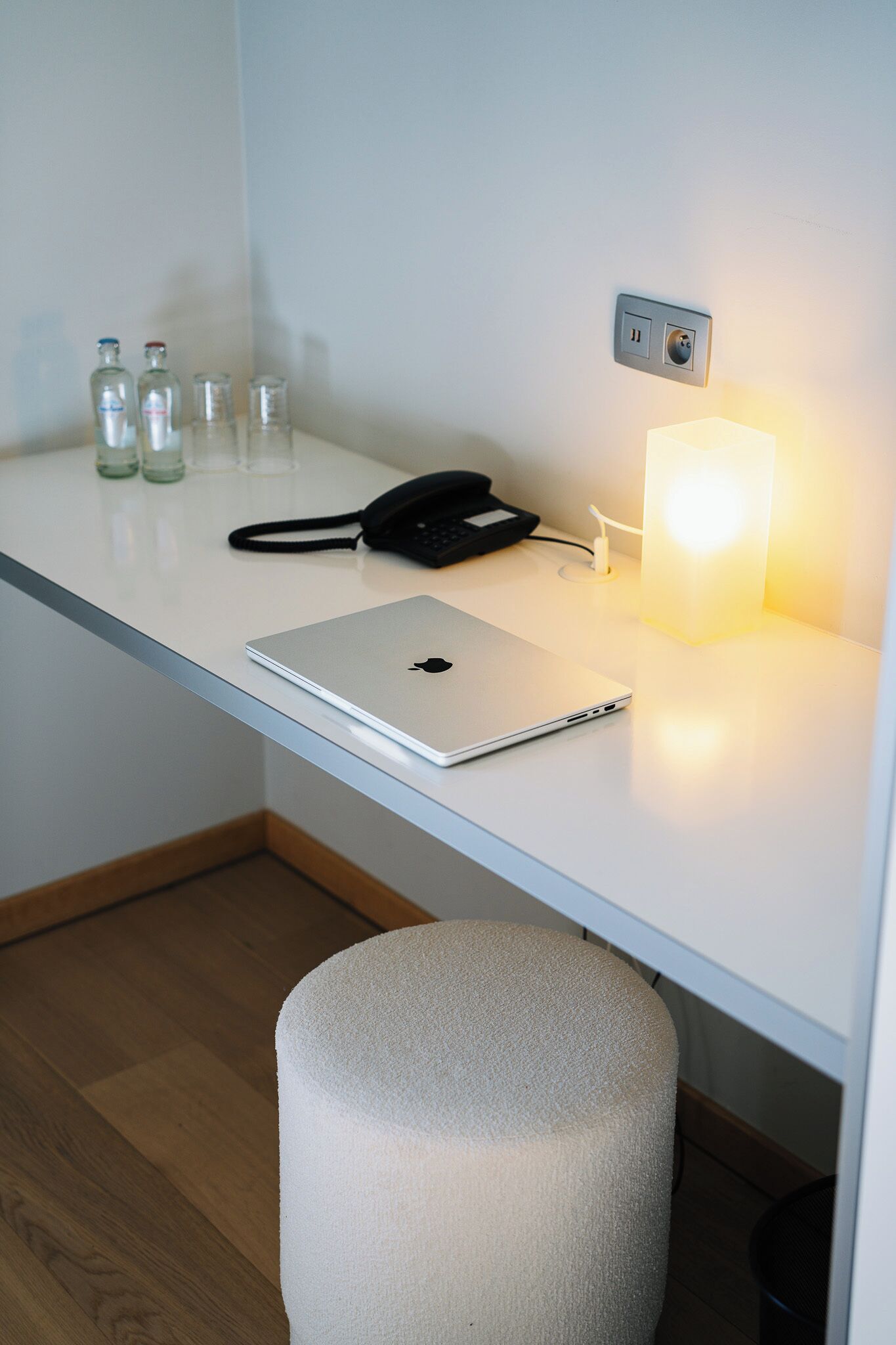 Una scrivania con un laptop, un telefono e una lampada. Ci sono anche diverse bottiglie di vetro sulla scrivania.
