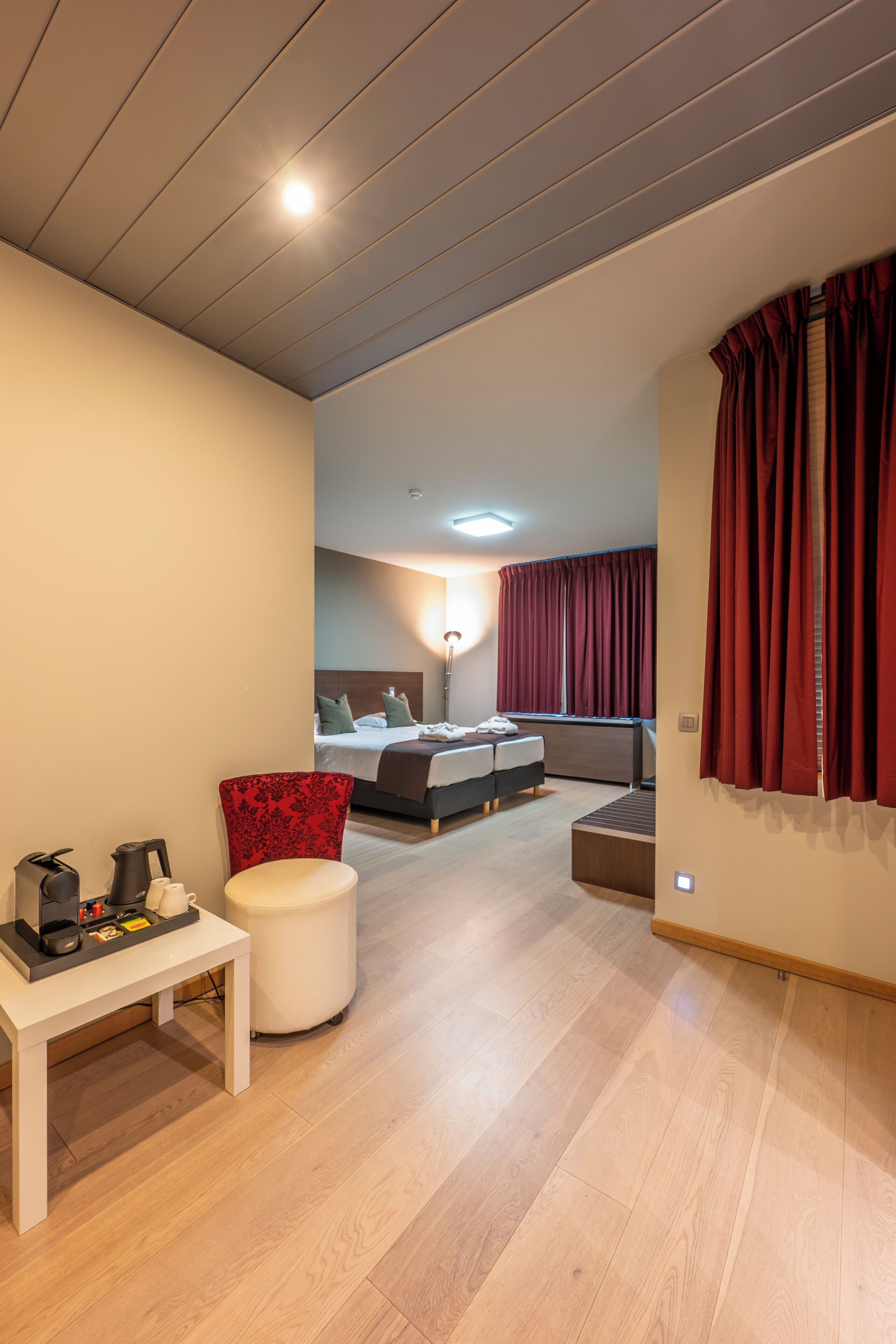 A modern hotel room with a bed, a desk, a chair, and a small table with a kettle and cups.