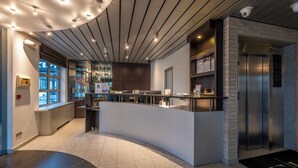A modern hotel lobby with a curved reception desk, a glass wall offering a view, a small kitchen area, and a reception counter with a digital display. - Falko Hotel (Meise)