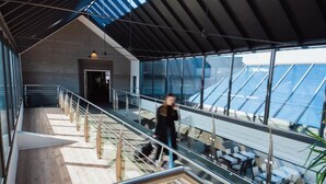 A modern interior with a glass staircase leading to a seating area with tables and chairs. - Falko Hotel (Meise)
