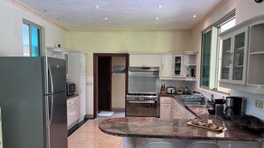 A modern kitchen with stainless steel appliances, a marble countertop, and two bar stools. - Paparadise, a haven of peace in the heart of Papara on the island of Tahiti. (Paparā)