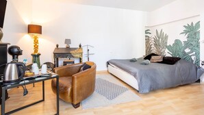 A bedroom with a bed, a chair, a table with a kettle, a lamp, and a wall with a plant mural. - L'Eclose - Kergoz, room in a private home in Guilvinec (Guilvinec)