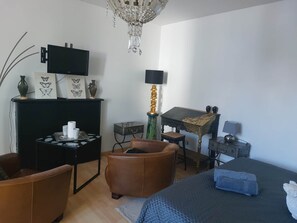 A bedroom with a bed, a desk, a chair, a television, a chandelier, and a small statue.