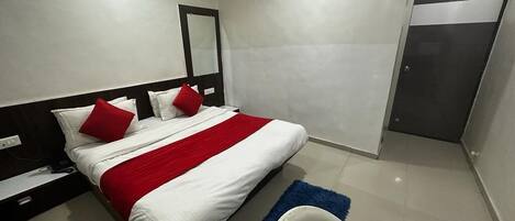 A modern hotel room with a large bed, a nightstand, a desk, and a wardrobe.