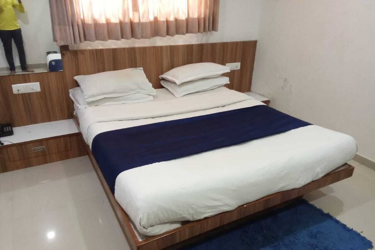 Un dormitorio con cama de madera, ropa de cama blanca, alfombra azul y una ventana con cortinas.