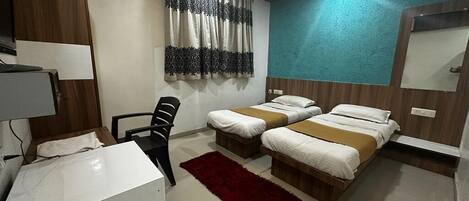 Une chambre d’hôtel avec deux lits, un bureau, une chaise, un tapis rouge et un ventilateur de plafond.