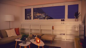 A modern living room with a city view, a sofa, a coffee table, a side table, and a bookshelf. - Luxury Nassa Penthouse with Private Terrace in Lugano (Lugano)